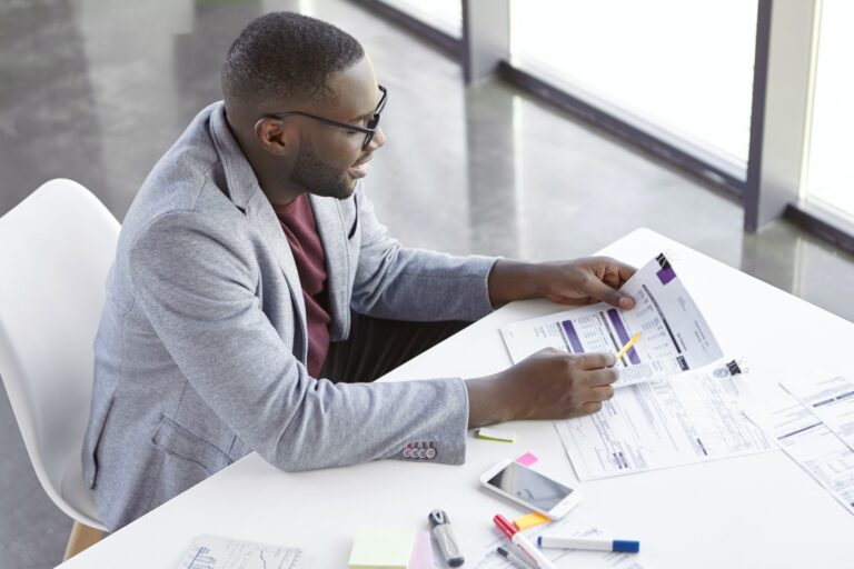 top-view-of-dark-skinned-african-male-copywriter-or-enterpreneur-looks-attentively-at-documents-stu